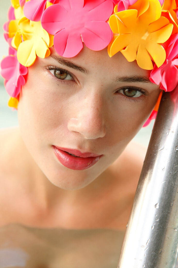 A woman wearing makeup with a colorful bathing cap looking into the camera