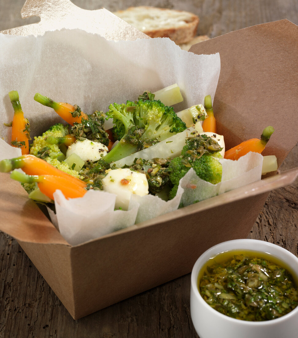 Warm vegetable salad in brown take out box with dip
