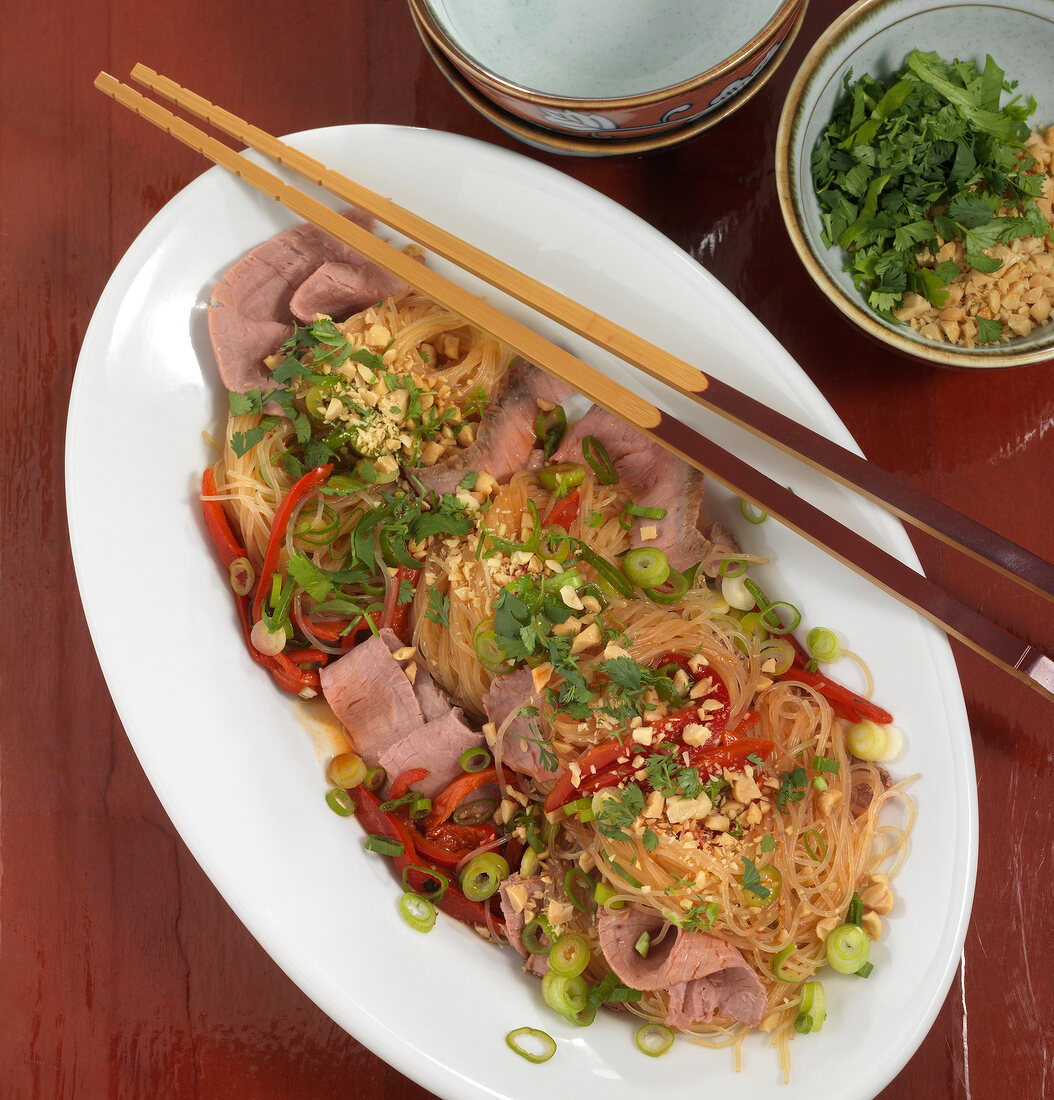 Glass noodle salad with peppers and chopsticks on plate, overhead view