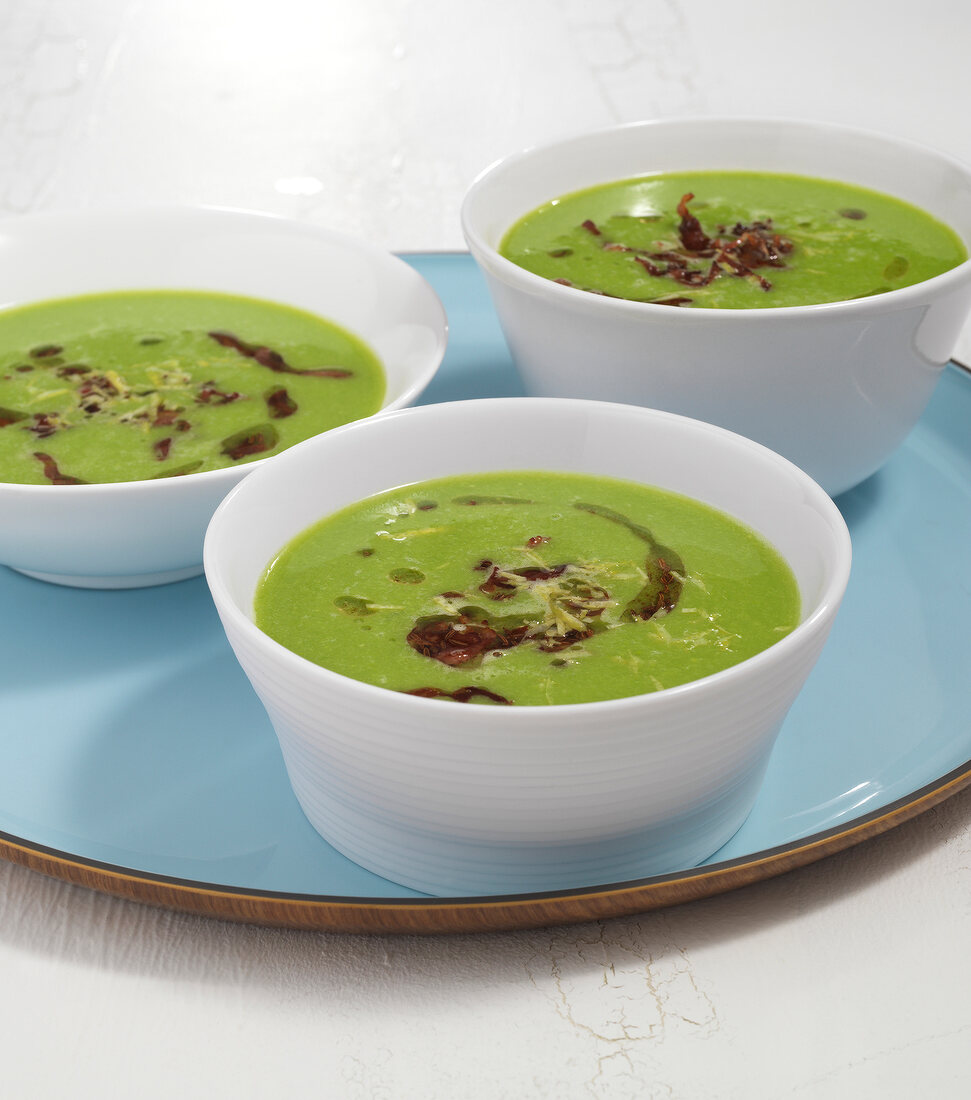 Close-up of three bowls of pea soup with bacon on plate