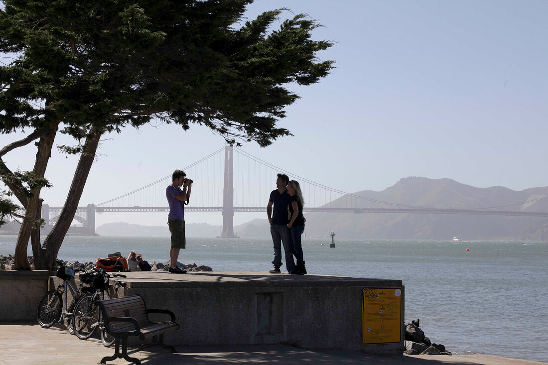 Man photographing couple in front of Golden Gate Bridge, San Francisco, California, USA