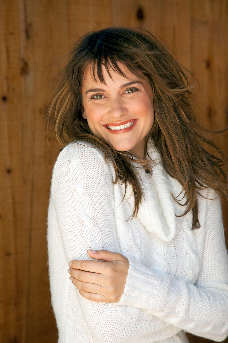 Happy woman in white turtleneck sweater standing in front of wooden wall and smiling