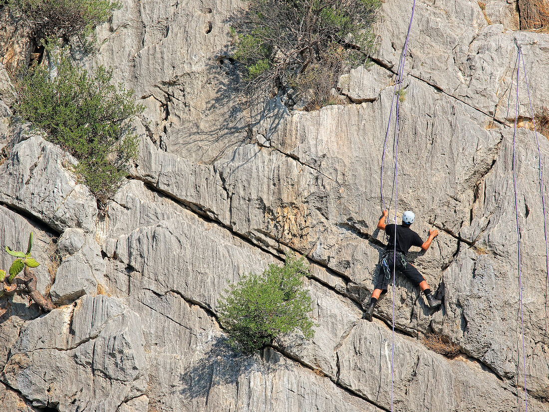 Man climbing rock mountain at Caletta Fuili, Cala Gonone, Sardinia, Italy