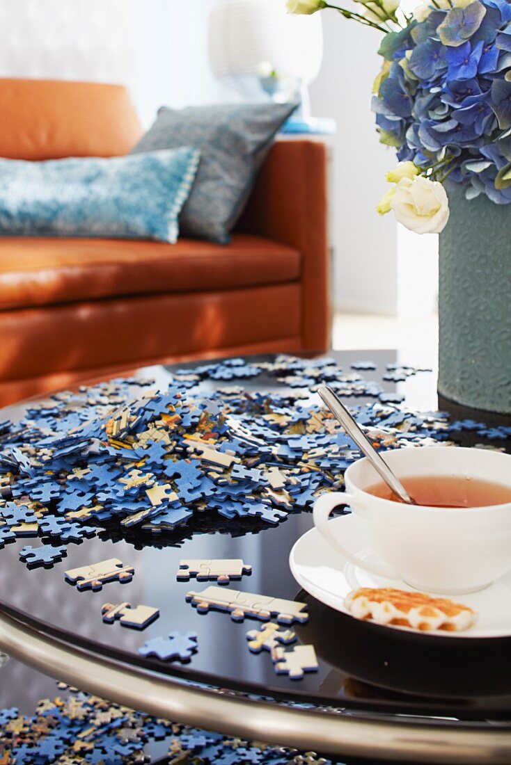 Jigsaw pieces and cup of tea on coffee table with leather couch in background