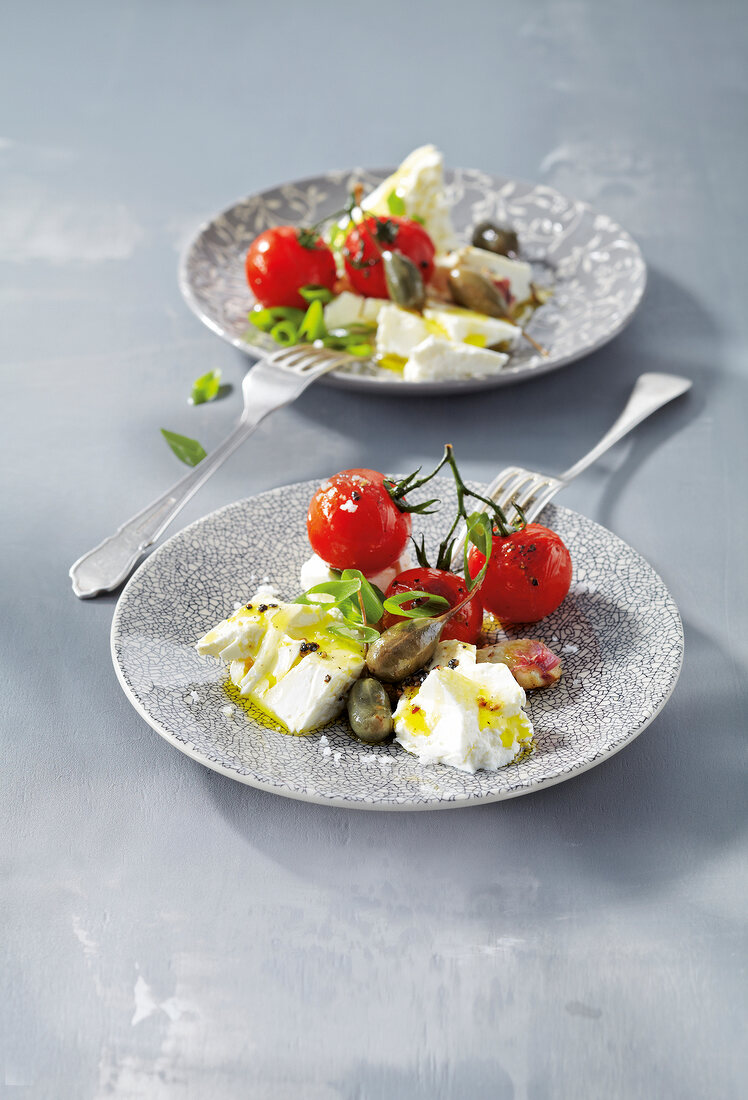 Warm tomato salad with layer of cheese and capers on plate