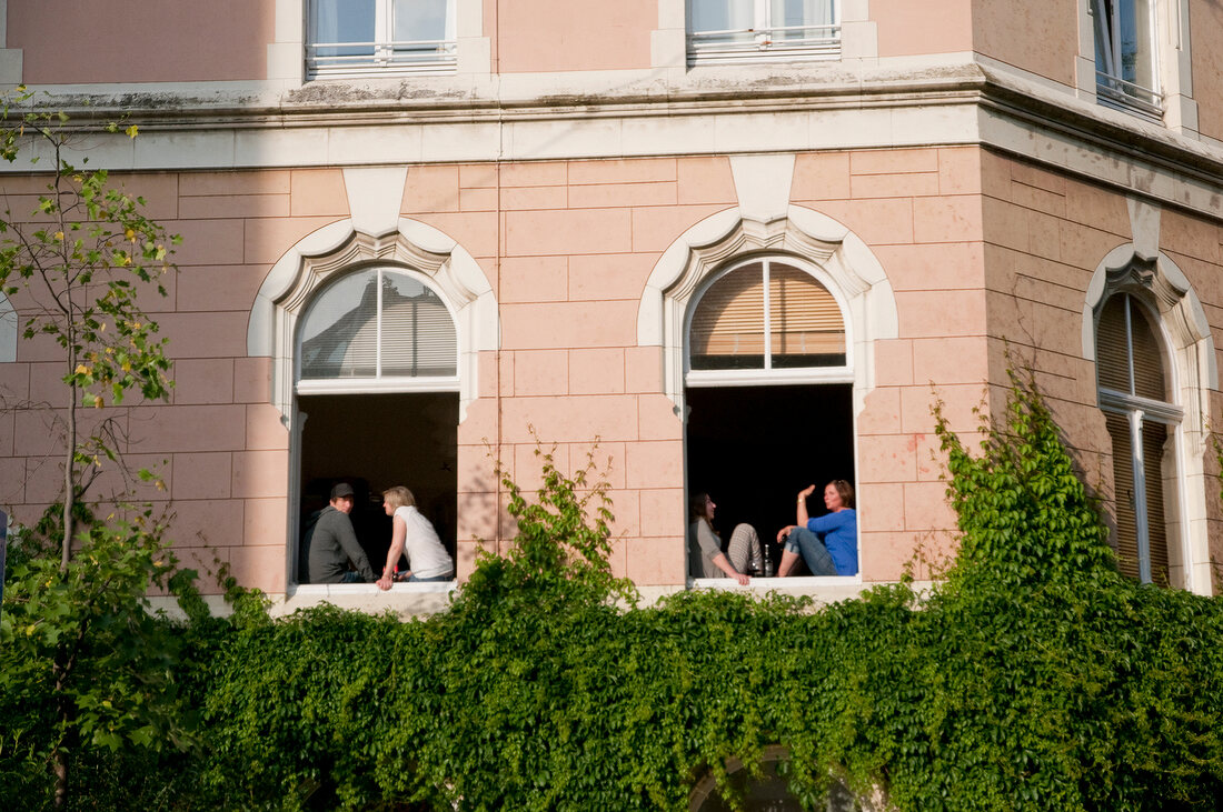 People sitting at window of building in Volksgarten street, Southtown, Cologne, Germany