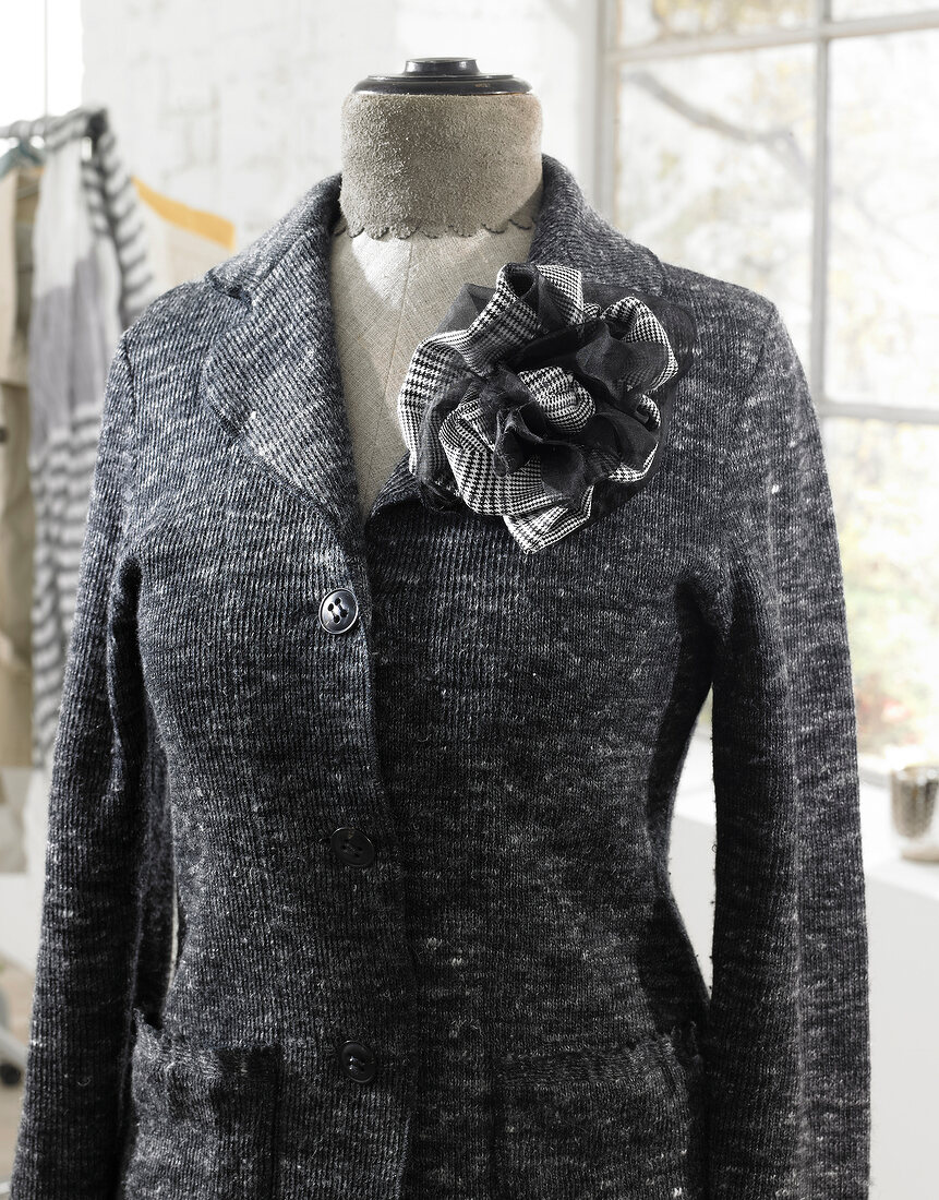 Fabric flower on collar of black knit blazer on mannequin