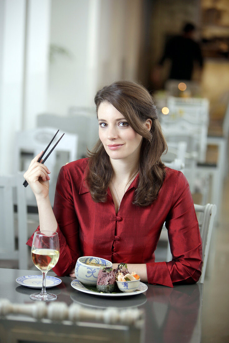 Portrait of woman eating with chopsticks and holding glass of white wine in restaurant