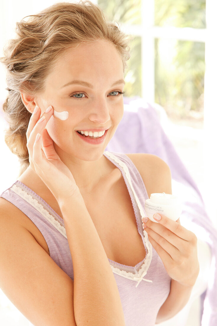 Woman with blonde hair applies moisturizer