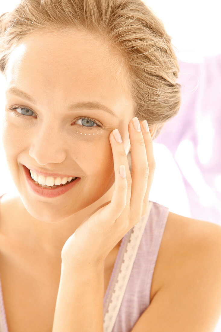 Woman with blonde hair applies eye cream