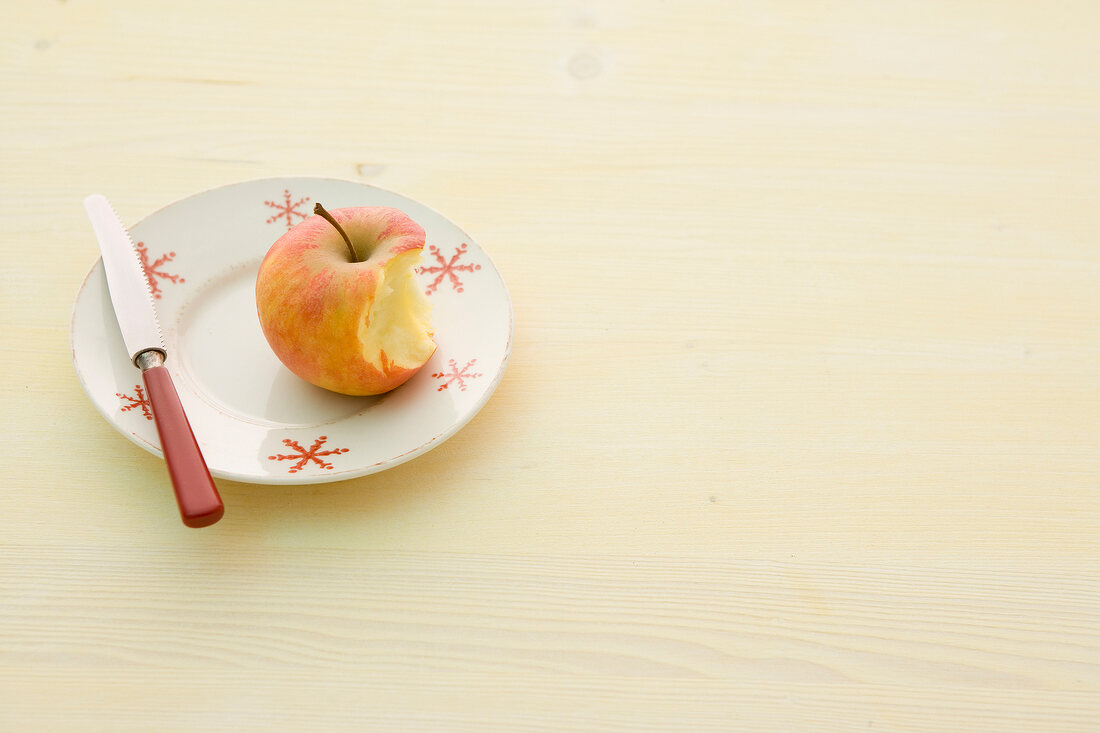 Bitten apple with knife on plate