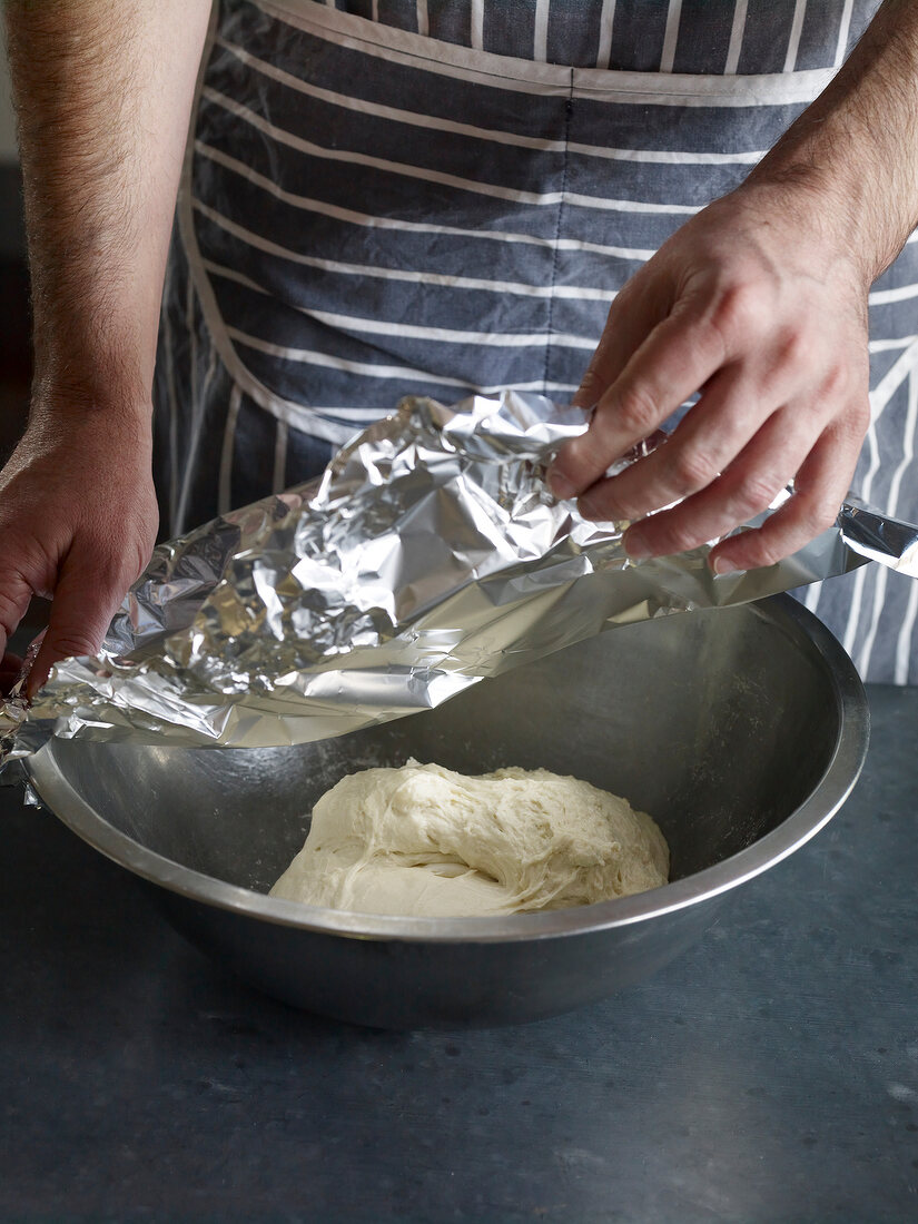 Close-up of hand covering bowl of dough with aluminium foil