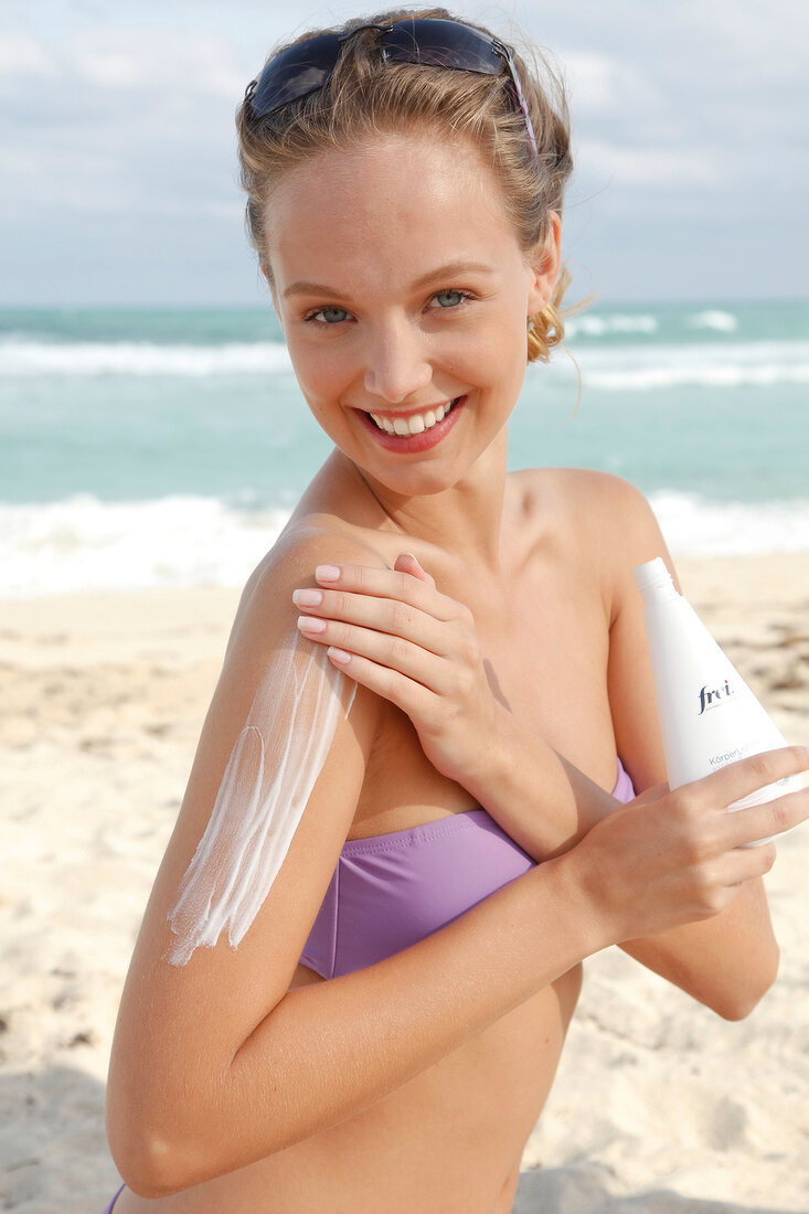 Frau mit blonden Haaren cremt sich den Oberarm am Strand ein