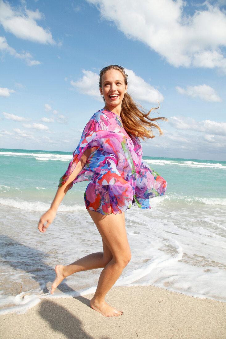 Carefree woman wearing floral patterned transparent blouse at beach, smiling widely
