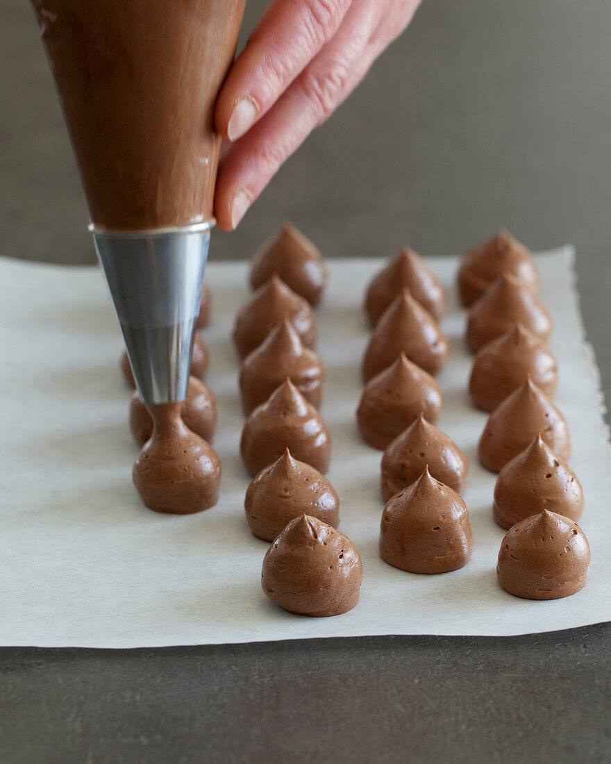 Dollops of truffle cream being made on baking paper with piping bag, step 1