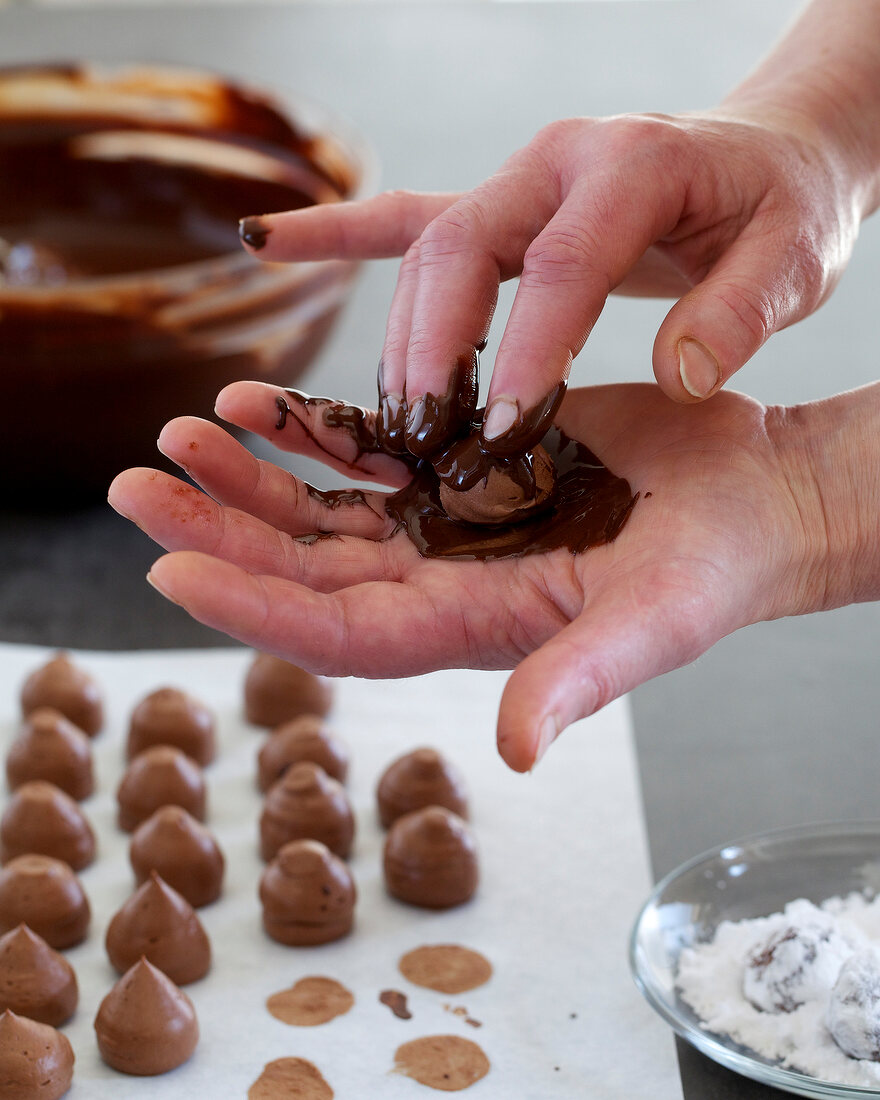 Close-up of hand coating dollops of truffle cream with melted chocolate, step 3