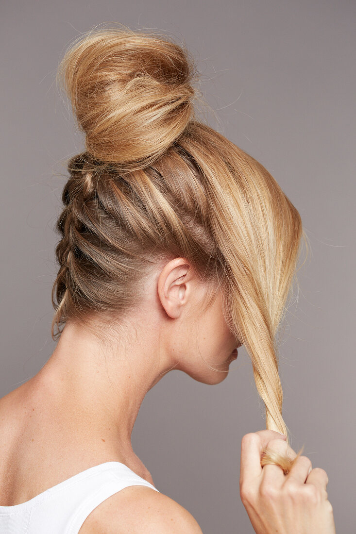Side view of blonde woman with hair bun twisting her hair to prepare updo hairstyle
