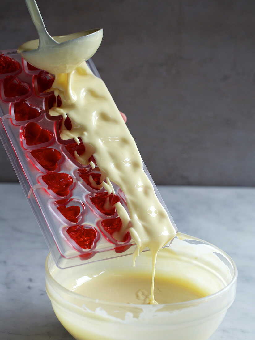 Melted white chocolate being poured in mould with red food colour, step 2