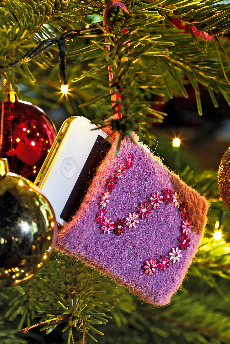 iPhone in Handytasche hängt am geschmücktem Weihnachtsbaum