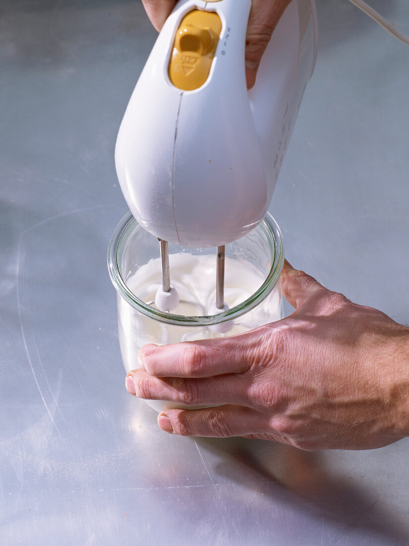 Mixing cream, egg whites and sugar in glass with hand blender