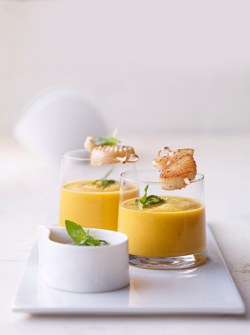 Glasses of lime and carrot soup with scallops on skewers