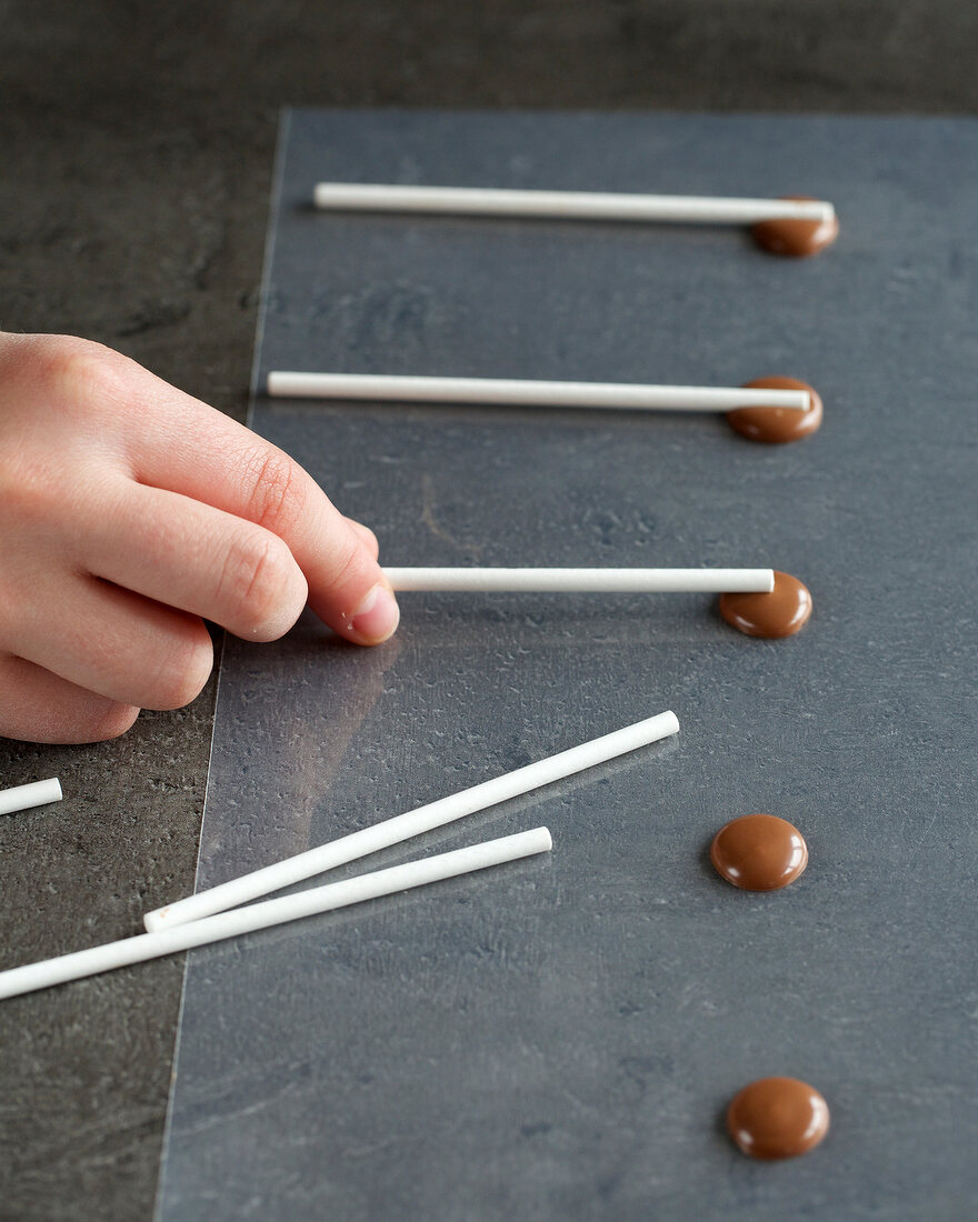 Small plastic pipes being placed on chocolate for preparing chocolate lollipops, step 2