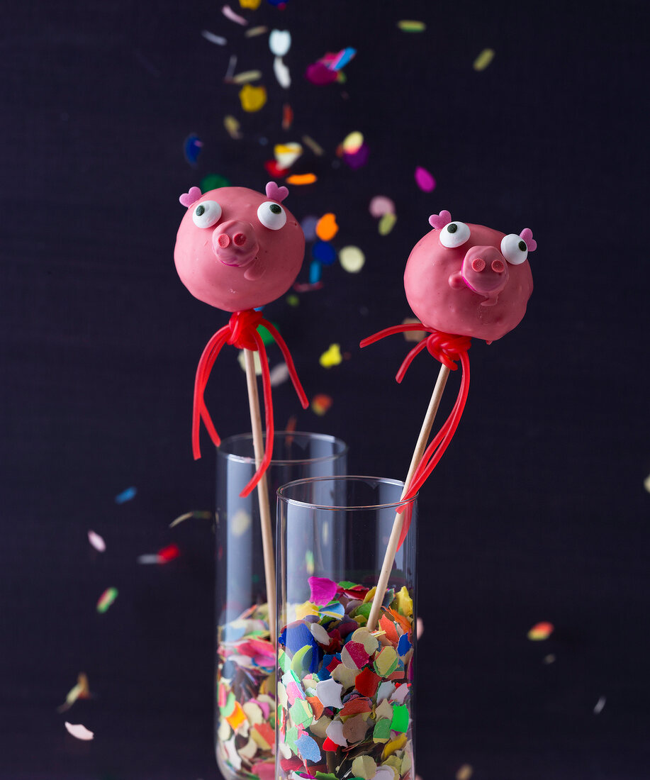 Pigs shaped cakes pops in glasses against black background