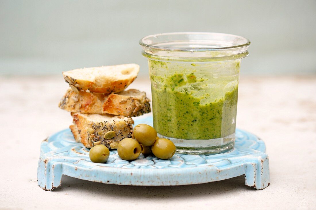 A jar of salsa verde, green olives and sliced of bread