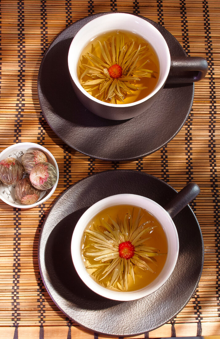zwei Teetassen, gefüllt mit Tee und Blütenkopf, Teeblumen