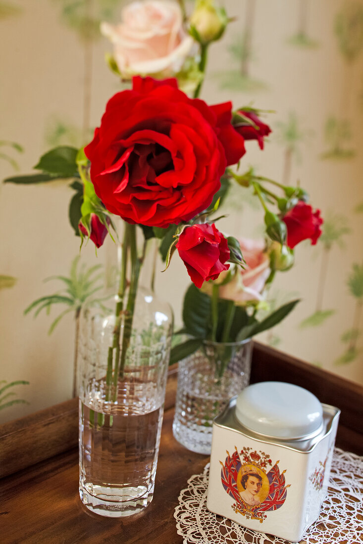 Roses in glass vase and tea caddy on wooden surface