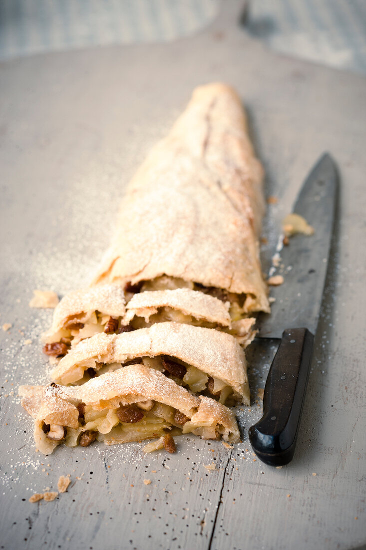 Slices of apple strudel with icing sugar and knife on wooden surface