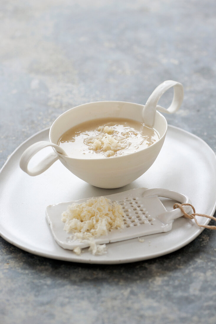 Horseradish soup in cup with grater on plate