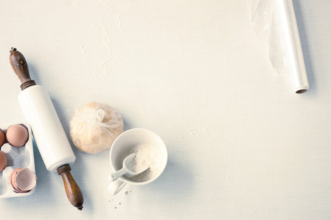 Various ingredients, dough, roller, eggs and foil paper on white background