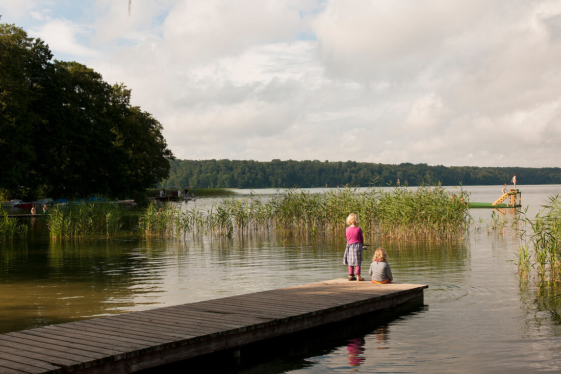Children standing at dock near Breiter Luzin lake, Germany