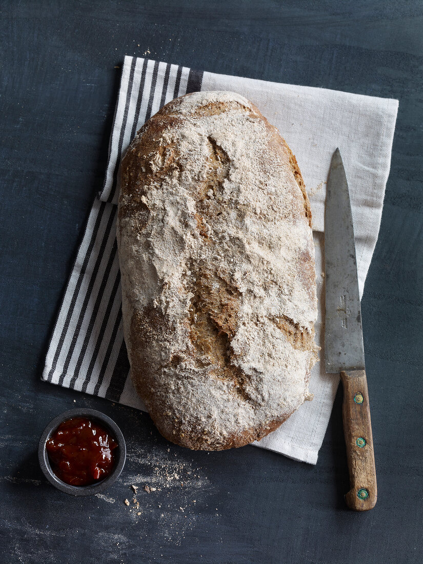 Brown bread with knife on tea towel and jam in bowl