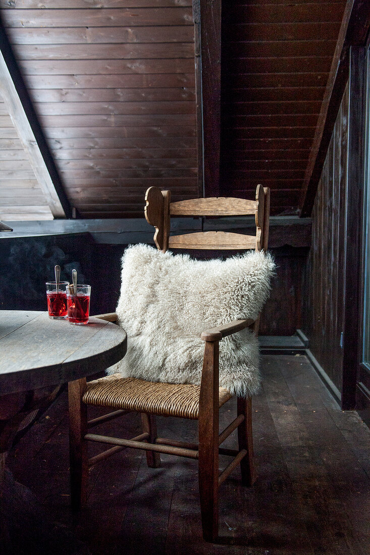 Wooden chair with fur pillows on balcony with beverage on wooden table
