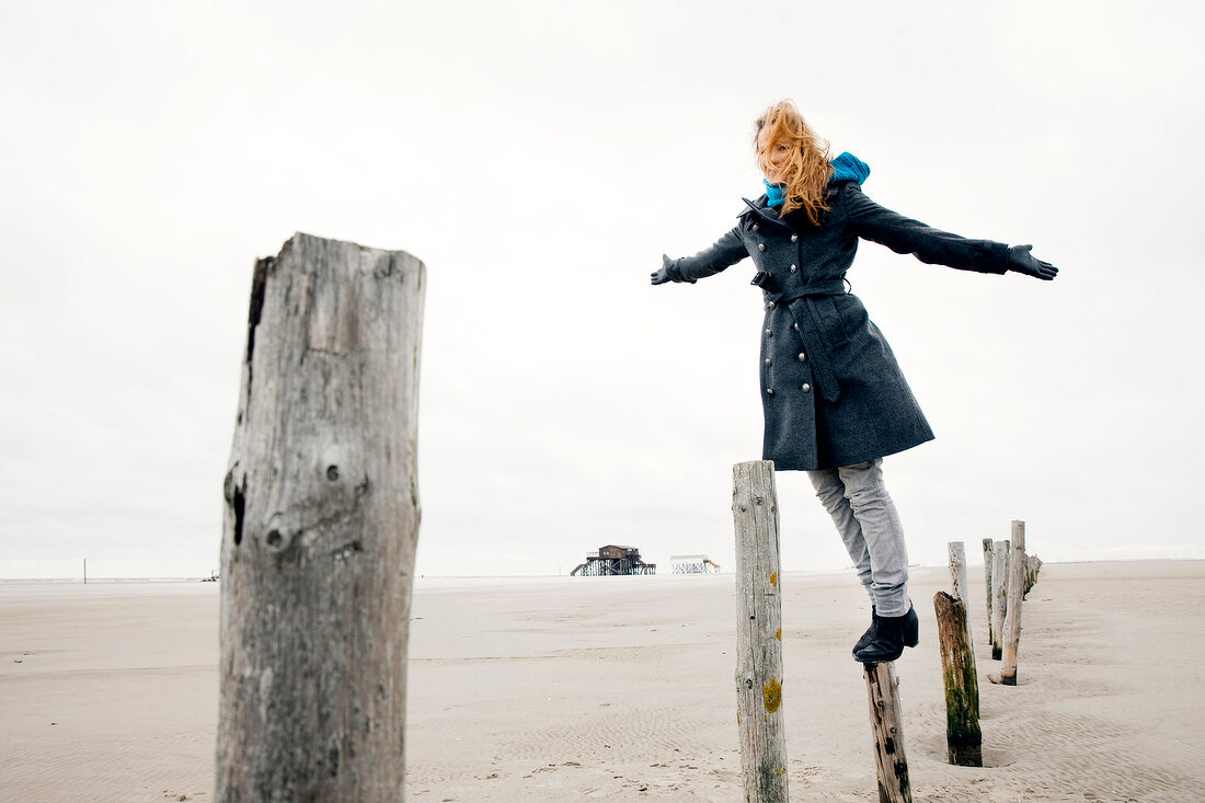 Woman wearing burberry coat balancing on stake at beach