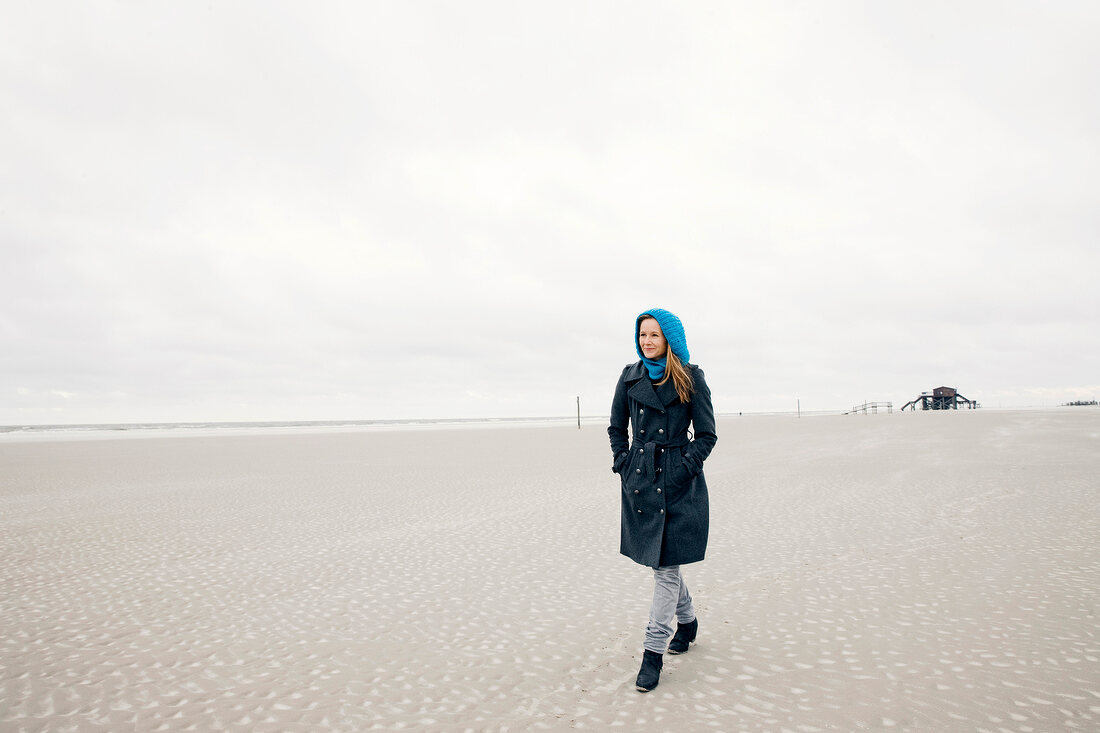 Woman wearing burberry coat standing relaxed on beach, wooden house in background