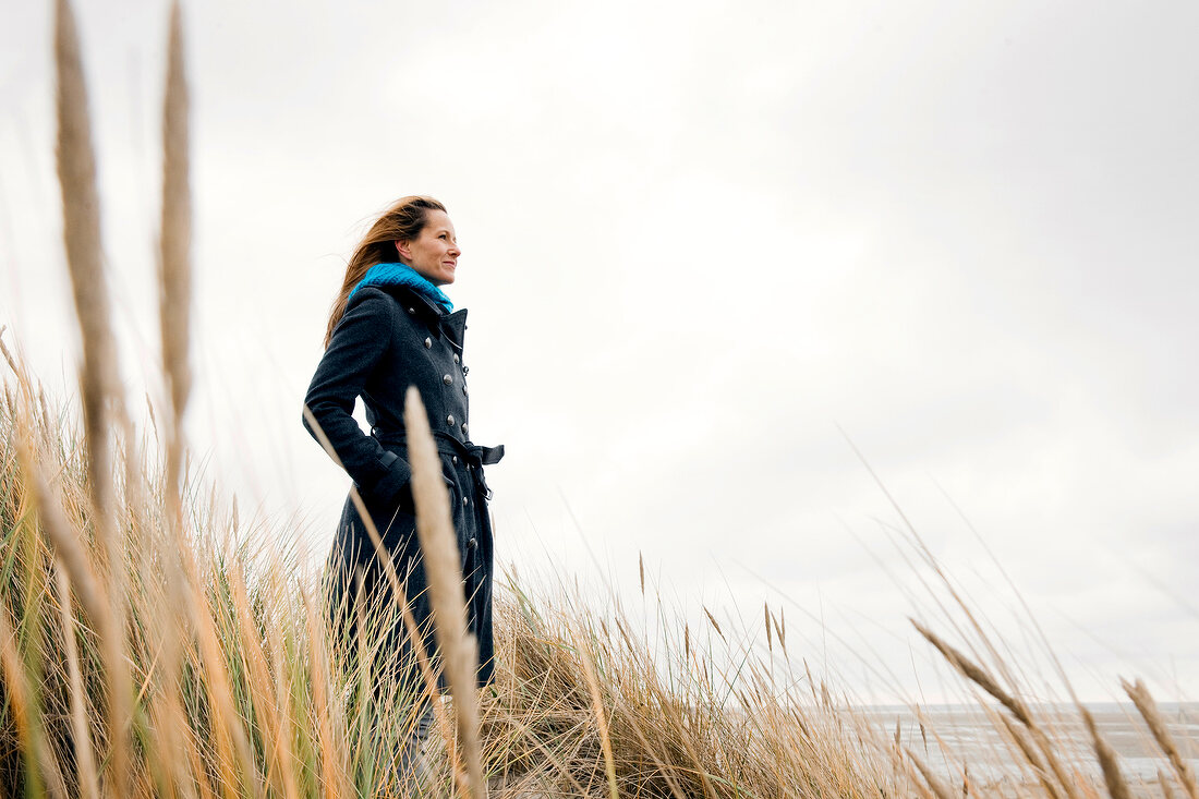 Woman wearing burberry coat standing relaxed between reeds on beach
