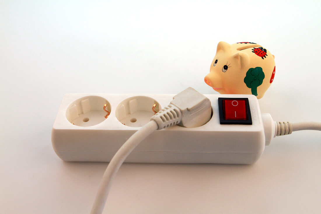 Close-up of triple plug extension with piggy bank on white background