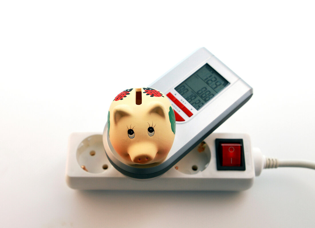 Close-up of triple plug extension with ammeter and piggy bank on white background