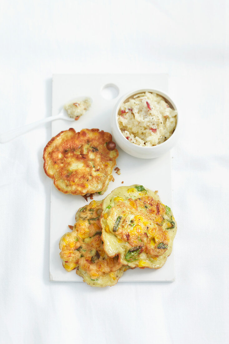 Three corn cakes and bowl of horseradish cream on white board