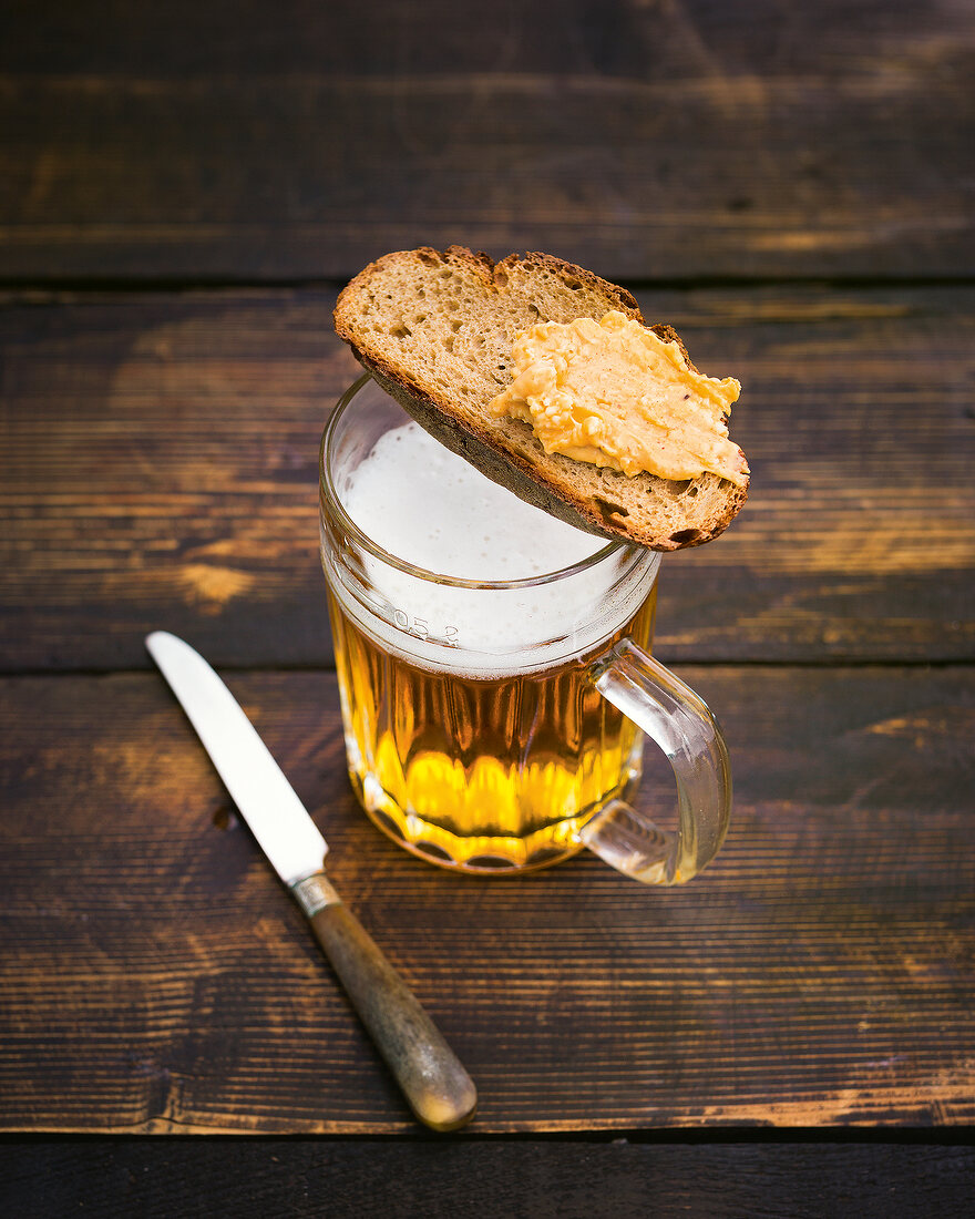 Brotzeit, Brotknust mit Obazda liegt auf gefülltem Bierkrug