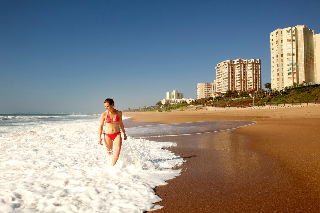 Woman in red bikini walking in water at beach at Umhlanga, South Africa