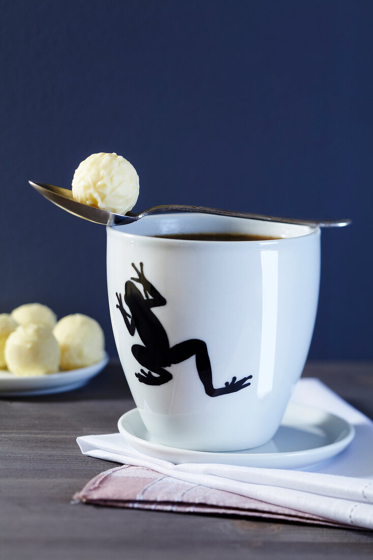 Close-up of coffee cup with frog motif and champagne truffle
