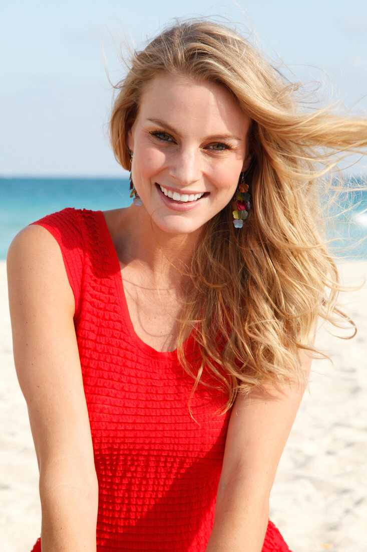 Blonde woman in a red dress on the beach, smiling and looking at camera