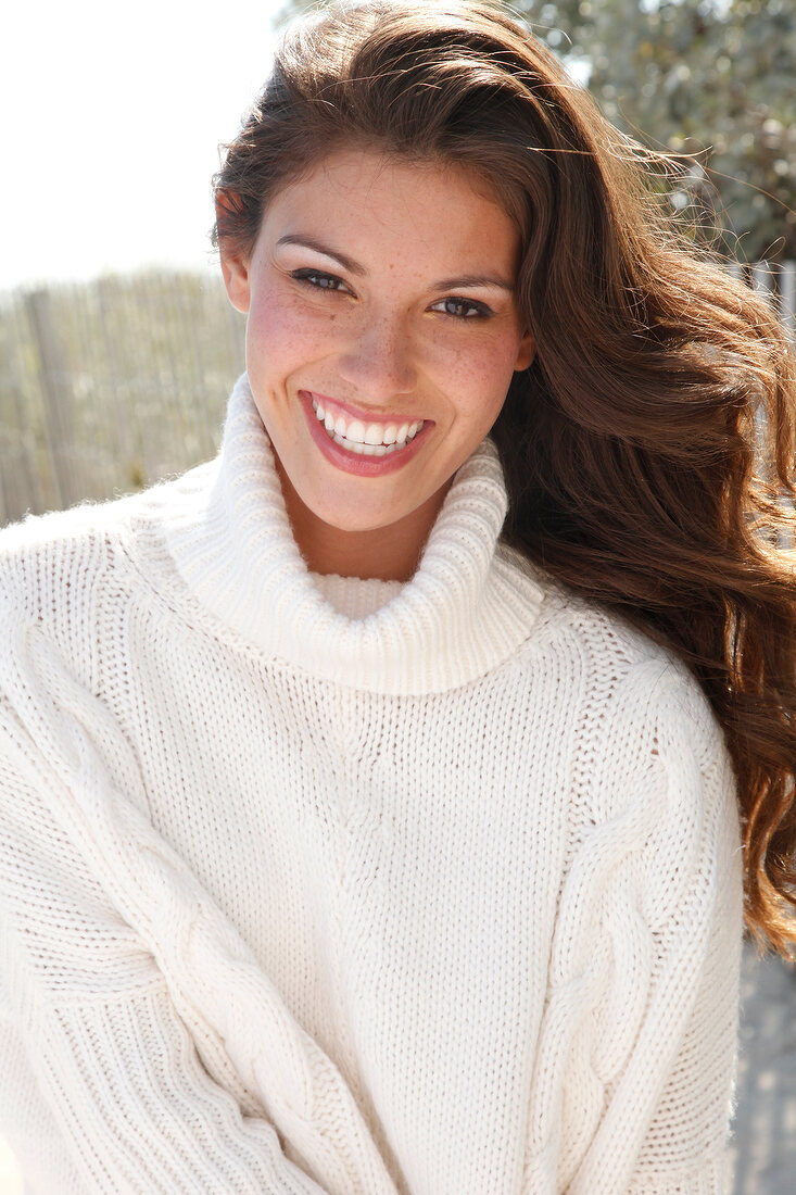 Dark-haired woman in a white turtleneck, laughing by the sea