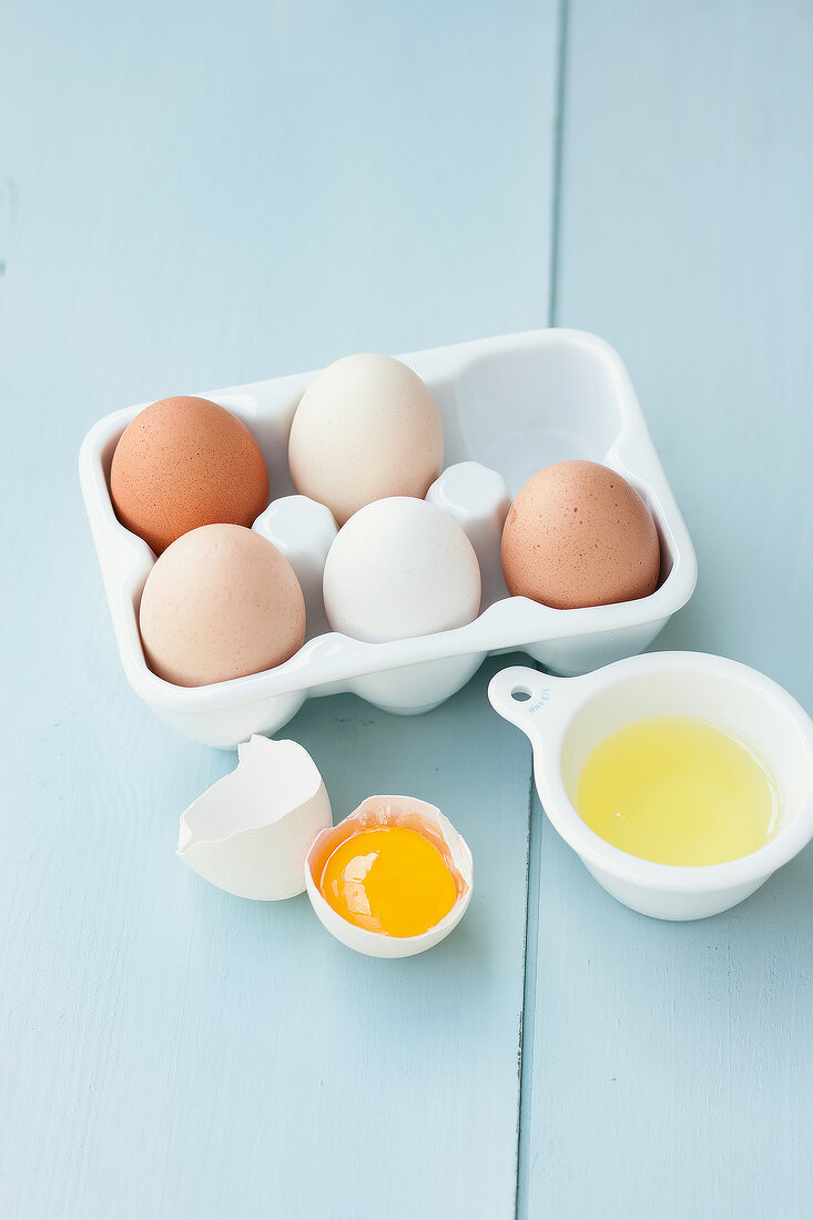 Carton with white and brown eggs and broken egg besides it