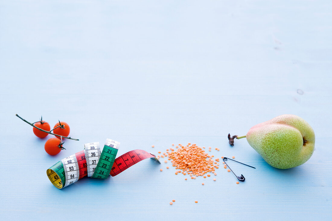 Tomato, pear, measuring tape and safety pin on blue background