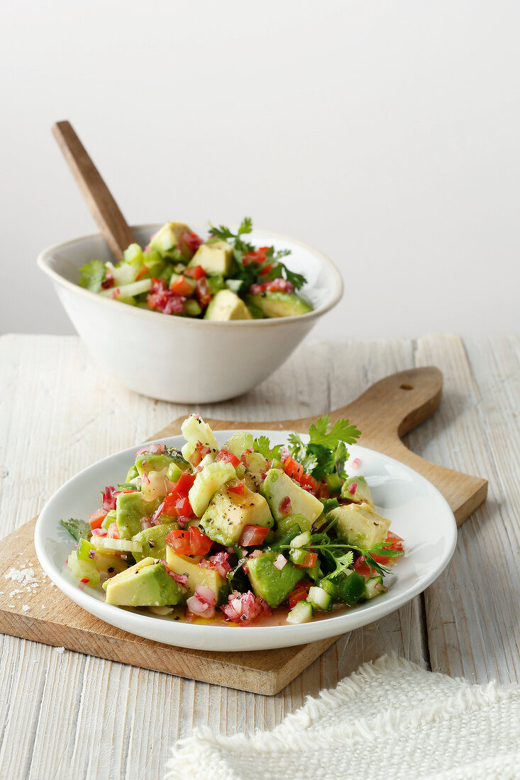 Plate and bowl of avocado salad on wooden board